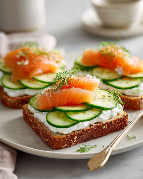 Three delicious open sandwiches with fresh salmon, sliced cucumbers, and cream cheese on whole grain bread, served on a light ceramic plate in a bright room