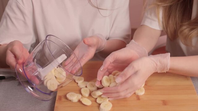 Women slicing bananas. Collaborative kitchen activity with ripe bananas and warm lighting. Two women engage in friendly banana slicing in particolored kitchen setting