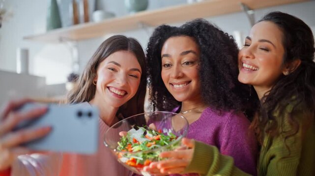 Smiling girls taking selfie cellphone holding salad standing kitchen closeup.
