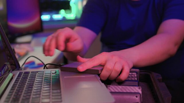 Professional IT technician working with external storage devices. Skilled IT professional performing quick data transfer on rugged external drives amidst ambient lighting