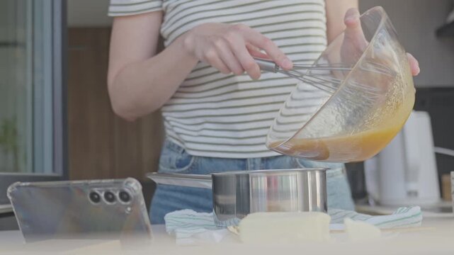 Woman turns on smartphone and adds whisked mixture from bowl into saucepan. Cooking tutorial and home baking content
