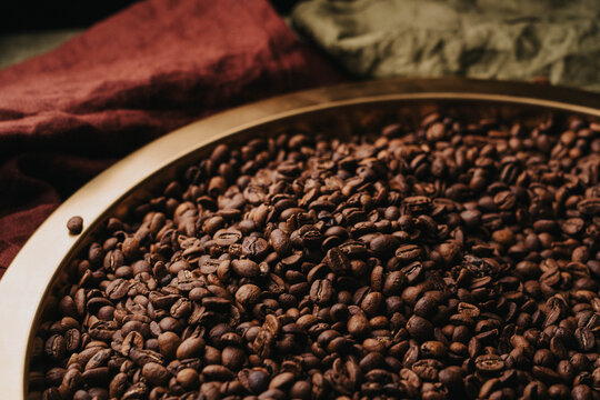 Granos de caf&eacute; reci&eacute;n tostados sobre charola dorada.