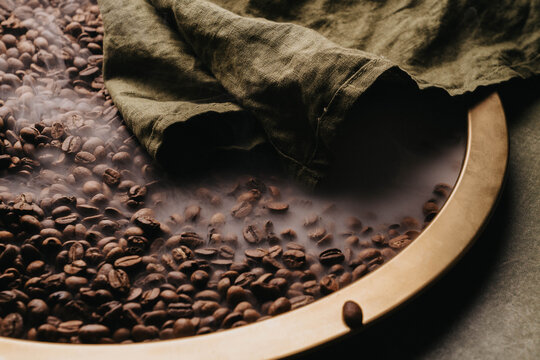 Granos de caf&eacute; reci&eacute;n tostados sobre charola dorada.