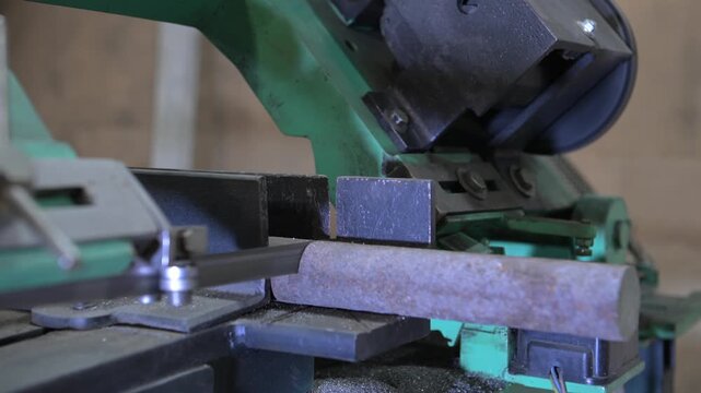 The lathe is in the production room. An electric metal cutting machine saws off a piece of metal with an automatic hacksaw to make a product