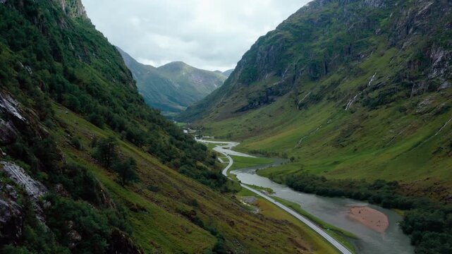 High-angle drone footage of majestic mountain peaks and a winding river road in Klakegg, Norway. Cinematic summer landscape featuring vehicles driving through a lush green glacial valley