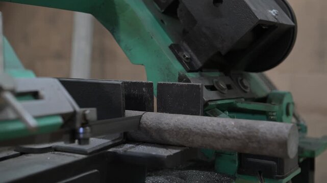 The lathe is in the production room. An electric metal cutting machine saws off a piece of metal with an automatic hacksaw to make a product