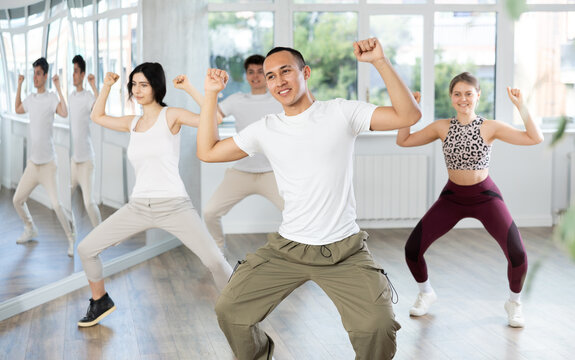 Emotional sporty young Asian dancer rehearsing modern krump dance moves during group workout in studio..