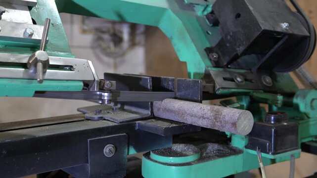 The lathe is in the production room. An electric metal cutting machine saws off a piece of metal with an automatic hacksaw to make a product