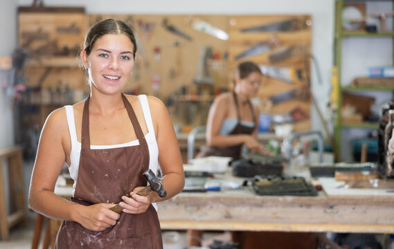 Happy young woman in pinafore standing in taller workroom full of tools