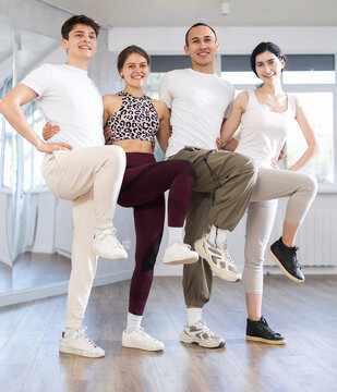 Multicultural group of enthusiastic cheerful young girls and guys traditionally lining in row while performing Greek sirtaki during dance class in sunny studio