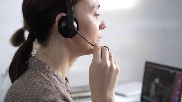 Focused female call center operator in brawn dotted blouse is assisting clients online, providing customer support and answering inquiries. Call center operators