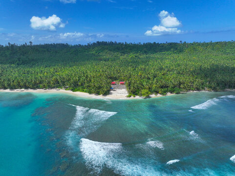 AERIAL: Small tropical cottages hidden between endless palms and reef break at Beng Bengs. Whitewater peels across the shallow shelf, turning this quiet beachfront into a classic Mentawai surf scene.
