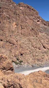 Ziz River winding through a deep rocky gorge with dramatic cliffs in the High Atlas Mountains of Morocco, Aa stunning scenic pan shot showing a shallow muddy river flowing through a dramatic deep