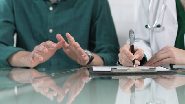 Doctor is writing notes on clipboard while listening to patient complaints during medical consultation in clinic office
