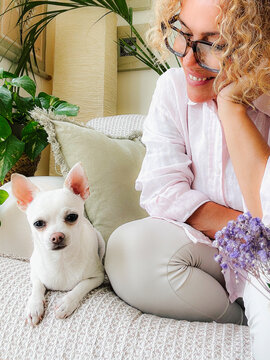 Woman smiling on couch with her small white chihuahua dog in a cozy home setting
