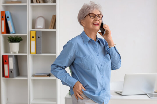 Happy senior businesswoman with laptop talking by mobile phone in office