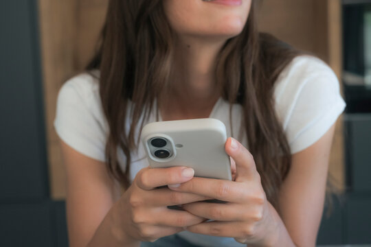 Young woman smiling and texting on smartphone while relaxing indoors in a casual white t-shirt
