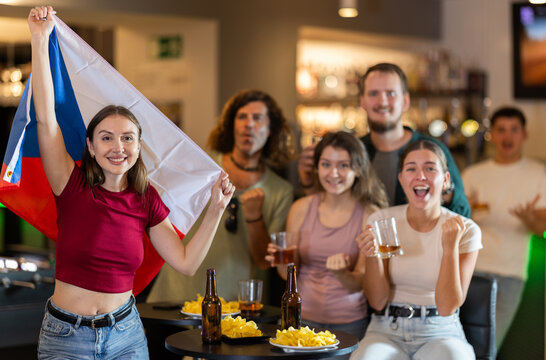 Men and women supporting Czech sports team in pub together. Happy group of friends raising Czech flag