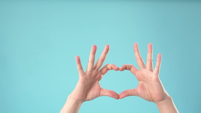 Hands making heart shape sign against blue background