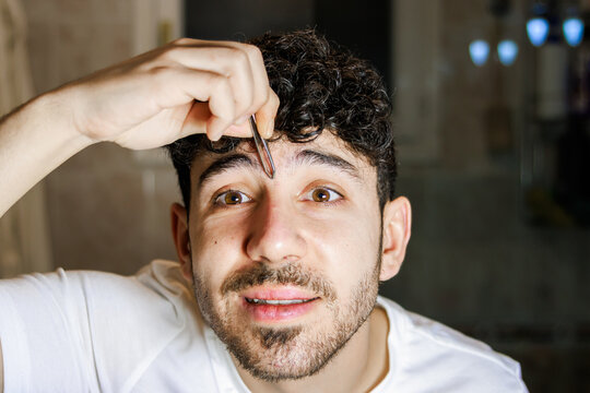 Young man plucking eyebrows for self-care and grooming, focusing on male beauty routine