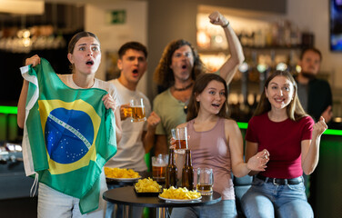 Obraz premium Brazilian fans with the national flag watch the match on TV and express various emotions
