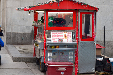 Fototapeta premium Red street food hot dog cart on downtown sidewalk with lit up open sign and menu with prices visible, Toronto May 2026