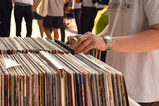 Young man searching through vintage vinyl records at outdoor street market in urban downtown area with sidewalk display and city atmosphere