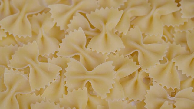 Uncooked pasta display. Farfalle cluster with shadows. Closeup of dry bow pasta shapes. Detailed view of dry farfalle pasta with shadows and textured background