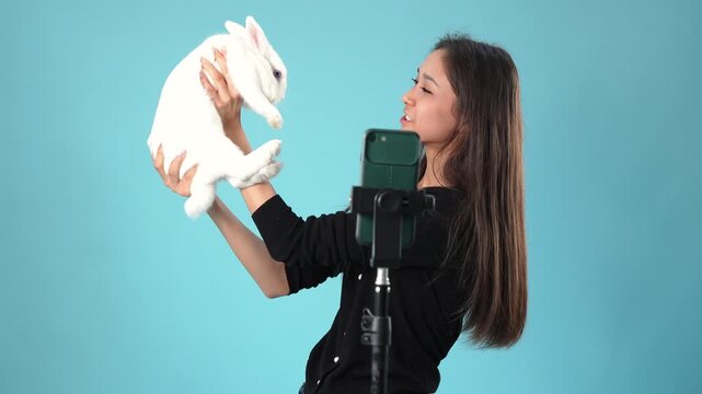Young female blogger recording video with cute white rabbit pet