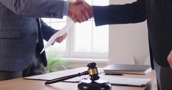 Male lawyer in suit make a deal and shaking hand with a man client standing at the desk on workplace in office with judge's gavel on table. Legal law and advice concept. 4k video. Slow motion.