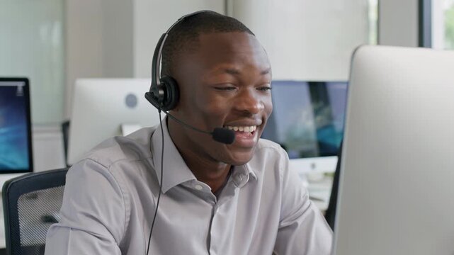 Smiling African American man working as a customer service representative in an office. Operator with headset talking on a call. Professional technical support agent communicating at a computer desk