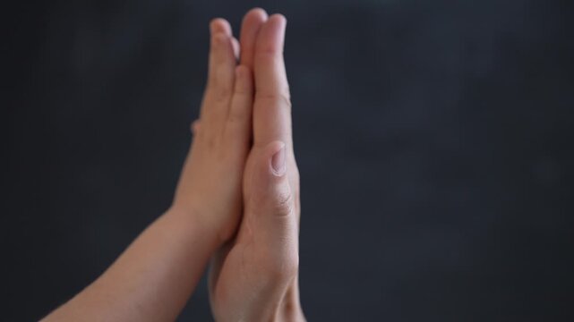 Parent and child giving high five close-up. Small hand touches adult palm on dark backdrop. Family hand bond showing trust and love. Parent palm meets child palm gently. Two hands connect with care.