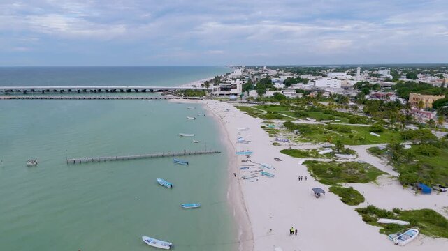 Aerial landscape shot captures a peaceful section of the beach in Progreso, Mexico. The foreground features a sandy path winding through coastal dunes and green scrub vegetation, where several small, 