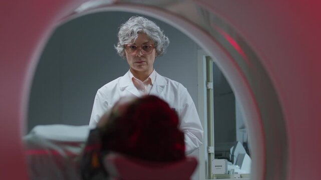 Experienced female radiologist in white coat watching patient leaving medical CT scanner after imaging procedure at clinic