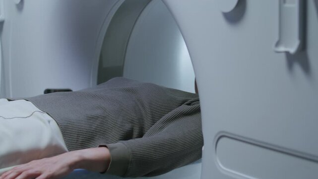 Mature female patient lying on motorized table, entering MRI scanner while radiology technician operating control panel during procedure at clinic