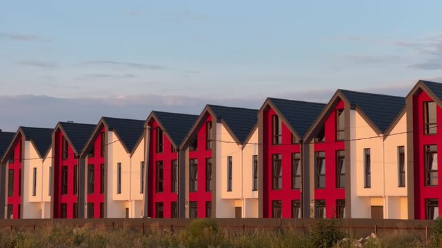 Pan Shot: Row of Newly Built Red and White Townhouses at Sunset in Suburban Area | Modern Residential Development with Gabled Roofs in Golden Hour Light | Real Estate Construction