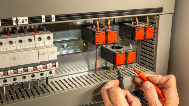 Electrical contractor engineer testing current transformers in an HVAC control cabinet. Electrician fault finding on transformers in an air conditioning and ventilation control panel.