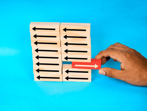 Hand inserting a red arrow block against opposite arrows, representing disruption, resistance, strategy conflict, and bold directional change.
