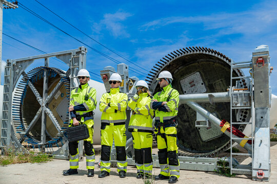 engineers in hard hats and high-visibility jackets inspect a massive piece of industrial equipment on a construction site, collaborating to ensure safety and proper assembly.