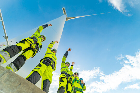 Team of engineers in reflective work suits inspect and demonstrate their work and success at a wind turbine power generation site.