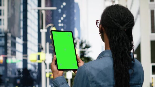 Vertical chroma key screen device used by freelancer in city downtown area, black woman using tactile touchscreen on a walk. Young adult in the metropolis with tablet, strolling around avenue.