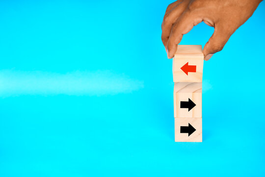 Hand holding a top block with an opposing arrow above stacked arrows, representing strategic conflict, direction change, and business realignment.
