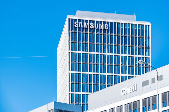 Modern office building with large SAMSUNG sign, glass facade, blue sky, South Korean tech giant headquarters, corporate architecture, electronics brand, business industry, corporate architecture
