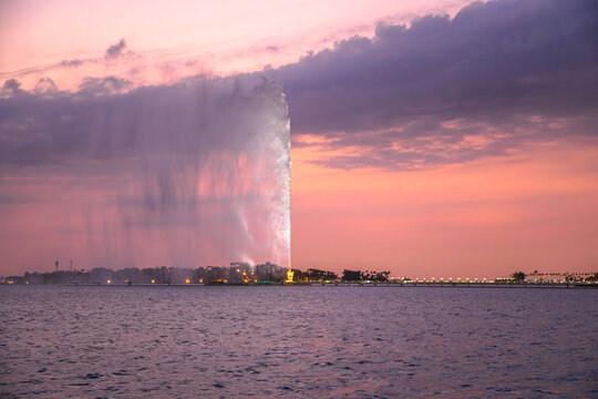 King Fahd's Fountain, the tallest fountain in the world, sprays water in the Jeddah Waterfront, Saudi Arabia, at sunset, with dramatic cloudy sky and calm sea