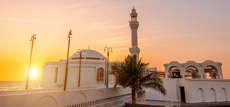 sun goes down on Al Rahmah Mosque on Jeddah Waterfront with JYC Jeddah Yacht Club building, on the Red Sea coast of Saudi Arabia, at sunset
