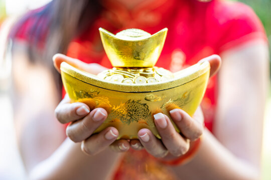 The traditional Chinese gold ingot or Sycee, a symbol of wealth and property, in the palms of a lady wearing a traditional Chinese blouse.