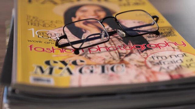 Many lifestyle magazines and glasses on wooden table, closeup. Camera moving forward