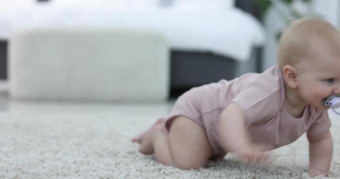 Cute little baby with pacifier crawling on floor at home