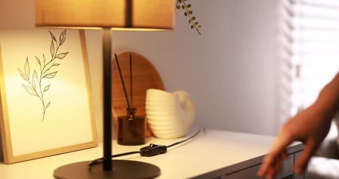 Woman turning on lamp with inline cord switch at cabinet near white wall indoors, closeup. Camera moving up