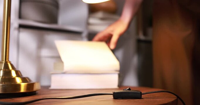 Woman putting book and turning off lamp with inline cord switch at wooden table indoors, selective focus